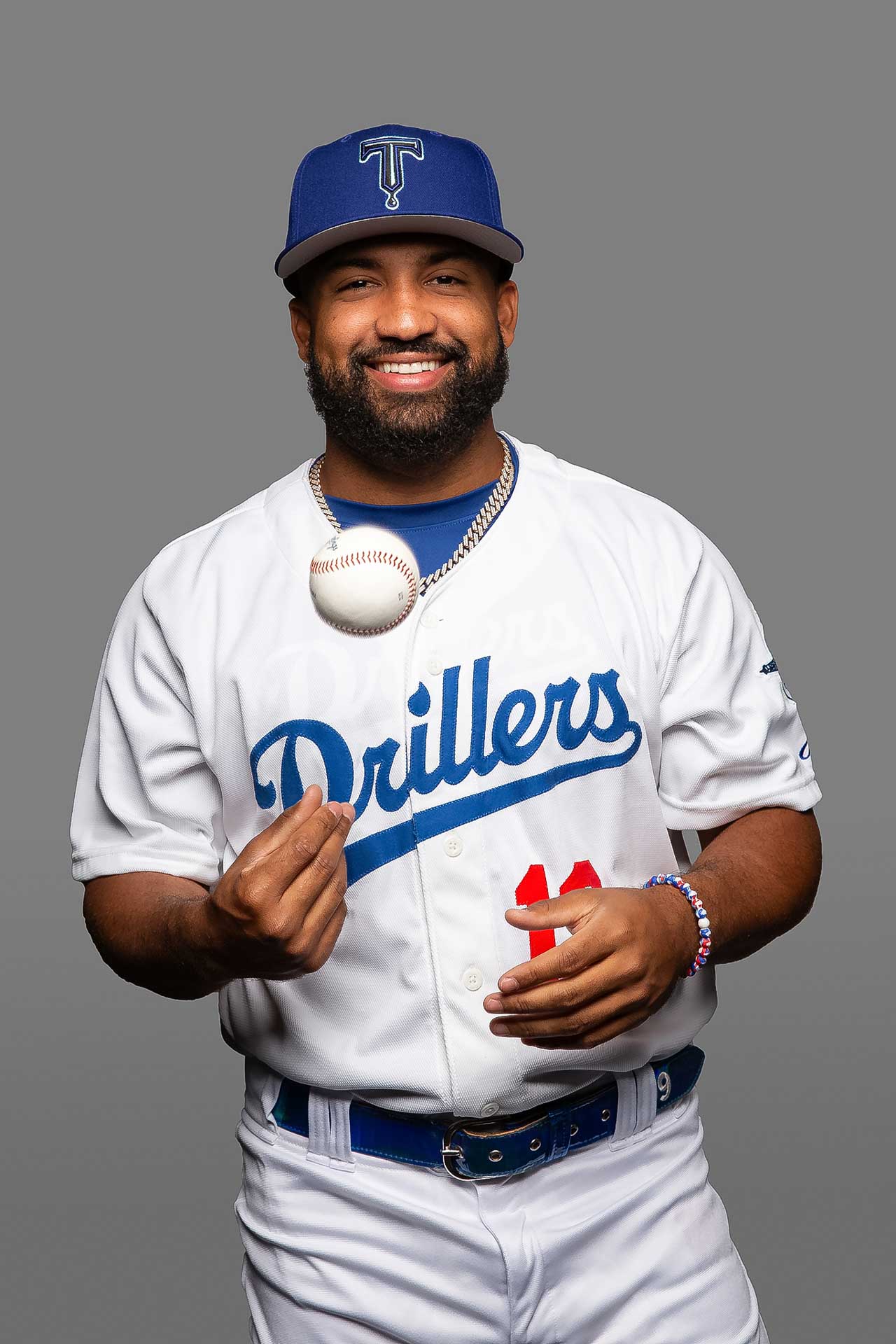sports portraits picture day tulsa293 tulsa drillers baseball player tossing a ball and smiling for his headshot photo on a grey background