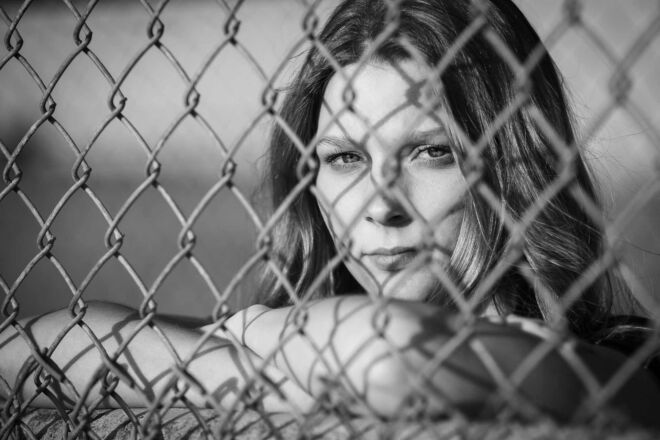 Young woman looking through a chain link fence