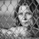 Young woman looking through a chain link fence