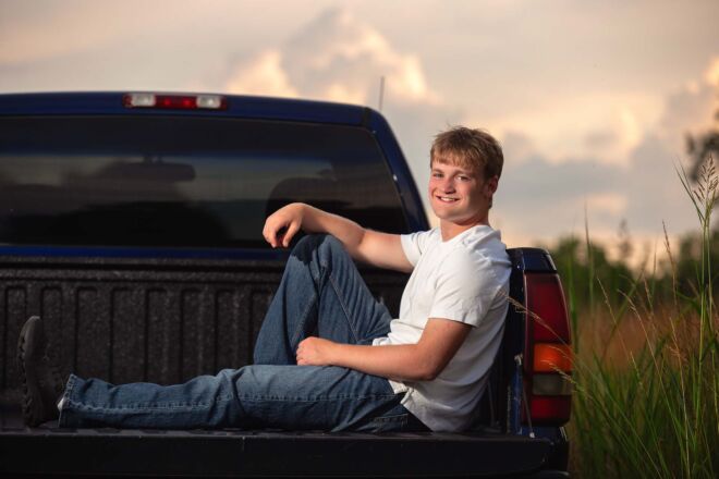 young man sitting in the back of his truck in a field at sunset