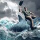young man riding a shark waving a cowboy hat